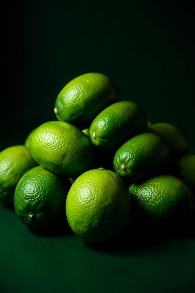 Fresh green limes, one sliced in half, on a light surface